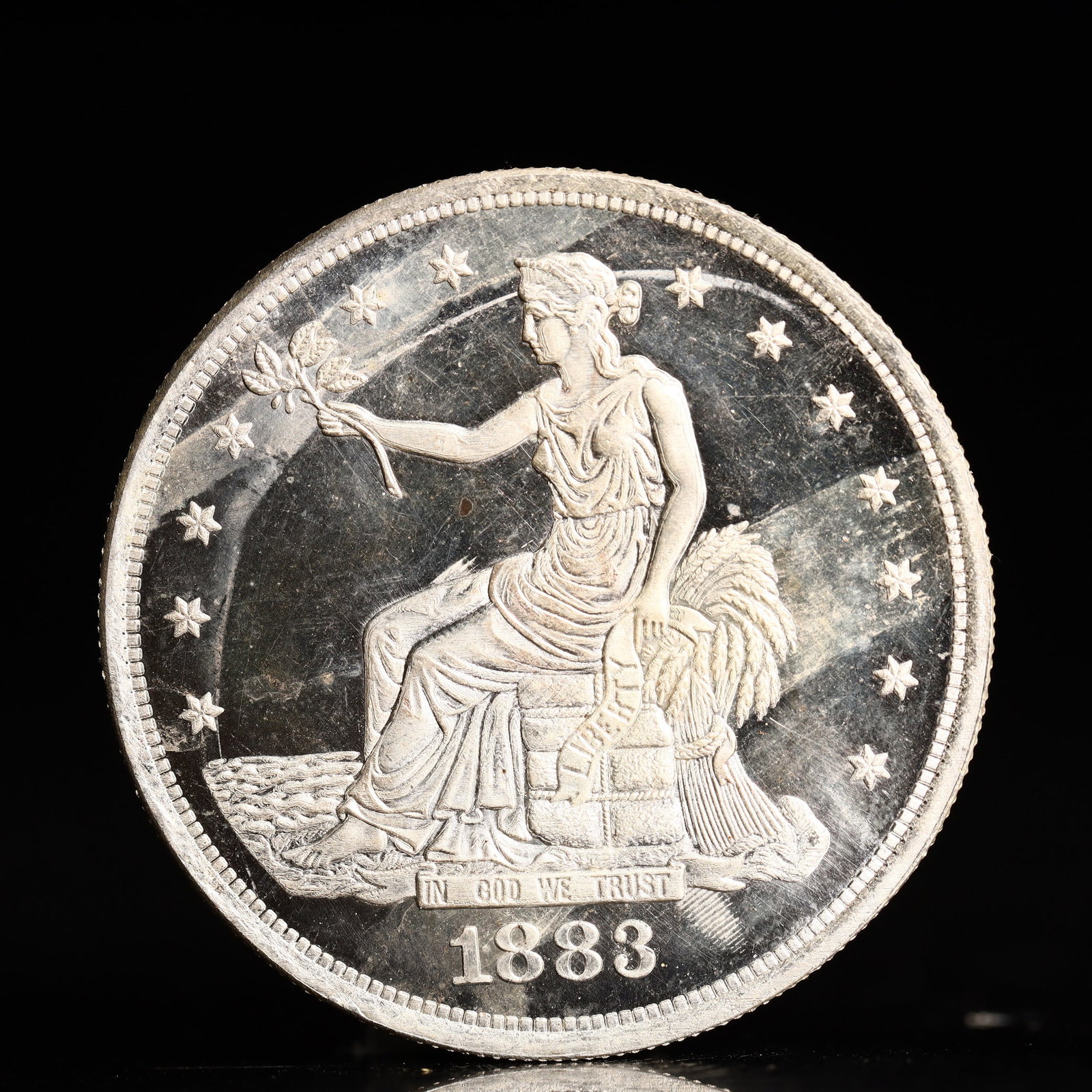 USA Trade Dollar 1883 Coin: American coin. Obverse: Liberty seated on a pedestal facing the sea to the left holding olive branches surrounded by 13 stars. IN GOD WE TRUST / LIBERTY / 1883. Reverse: An eagle holding branches with