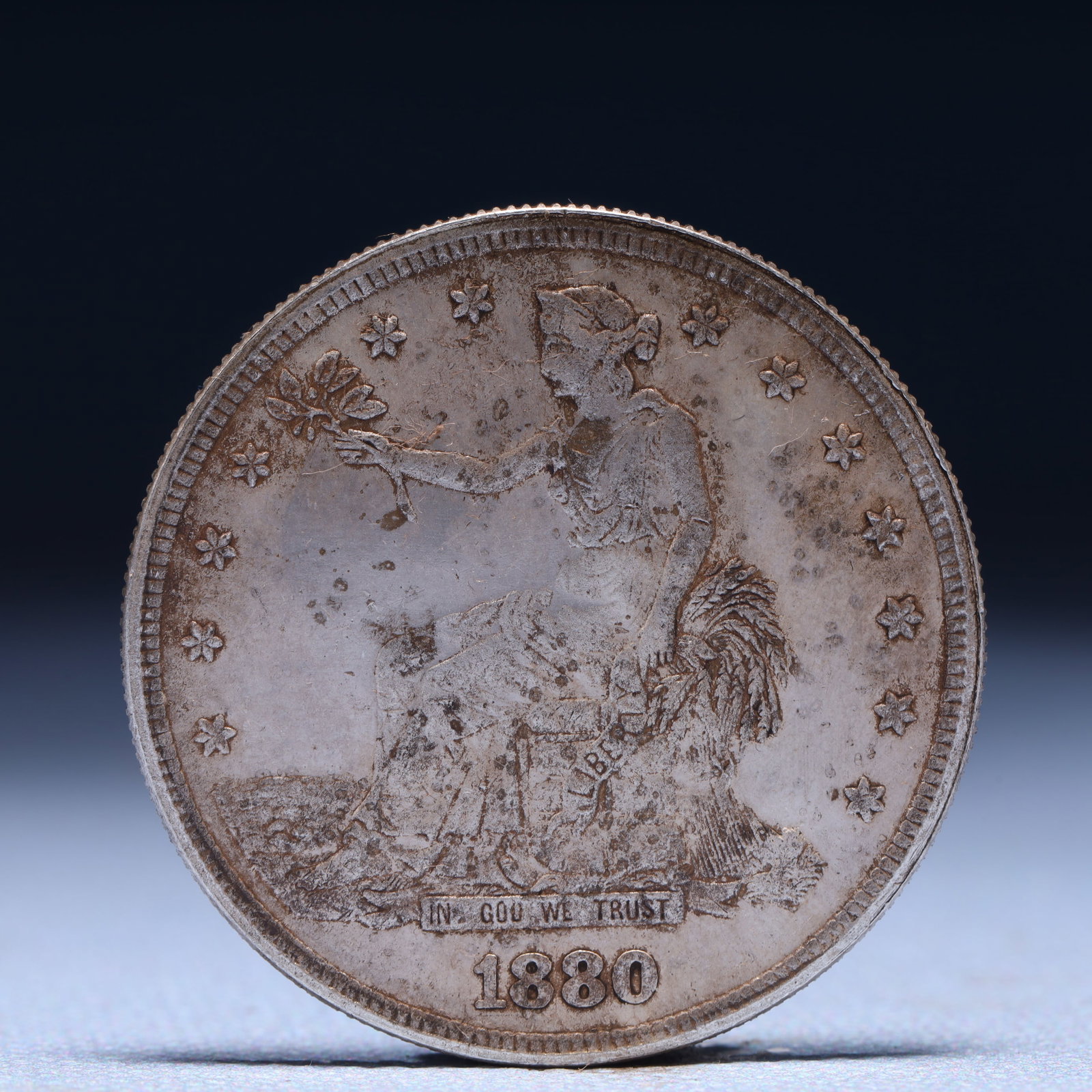 USA Trade Dollar 1880 Coin: American coin. Obverse: Liberty seated on a pedestal facing the sea to the left holding olive branches surrounded by 13 stars. IN GOD WE TRUST / LIBERTY / 1880. Reverse: An eagle holding branches with