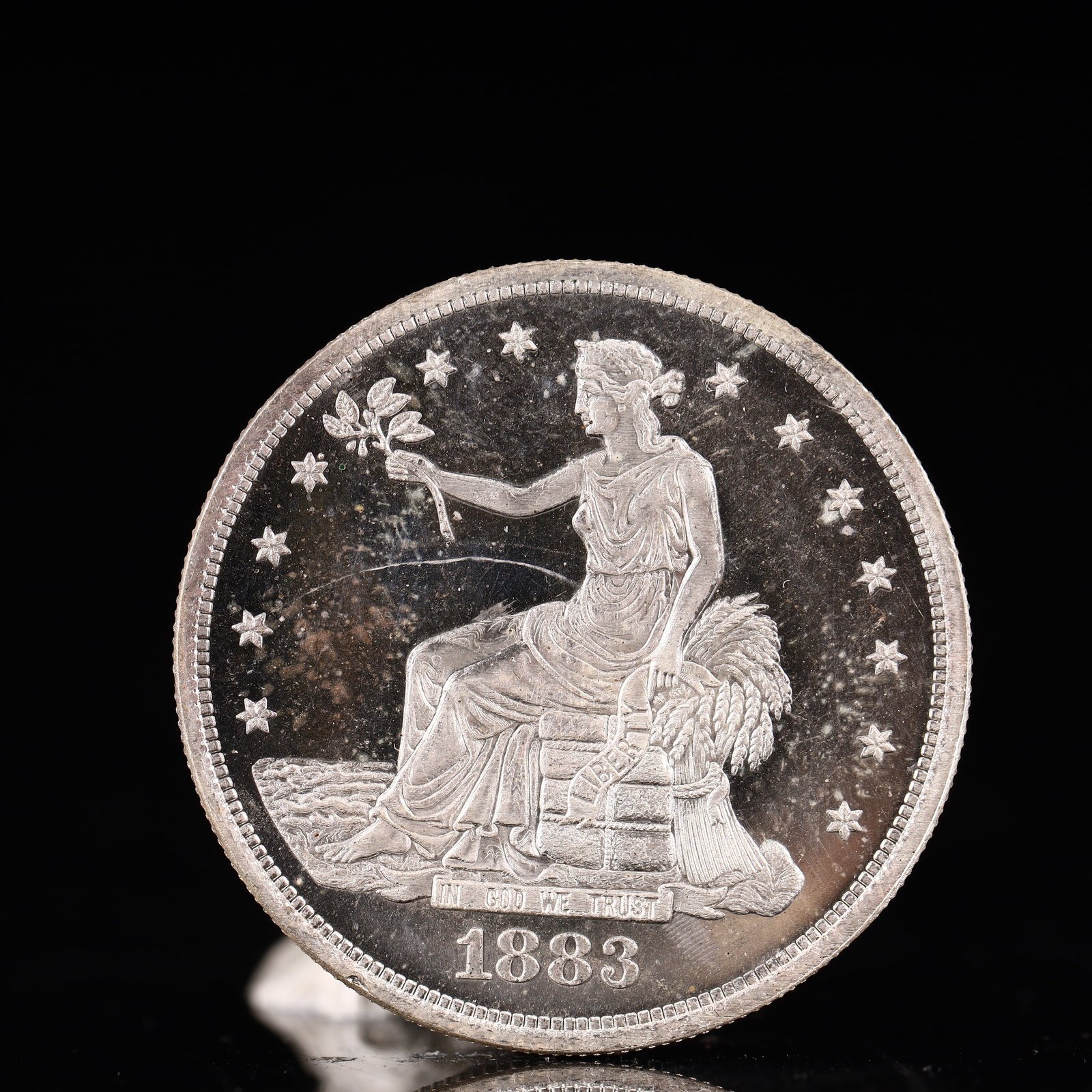 USA Trade Dollar 1883 Coin: American coin. Obverse: Liberty seated on a pedestal facing the sea to the left holding olive branches surrounded by 13 stars. IN GOD WE TRUST / LIBERTY / 1883. Reverse: An eagle holding branches with