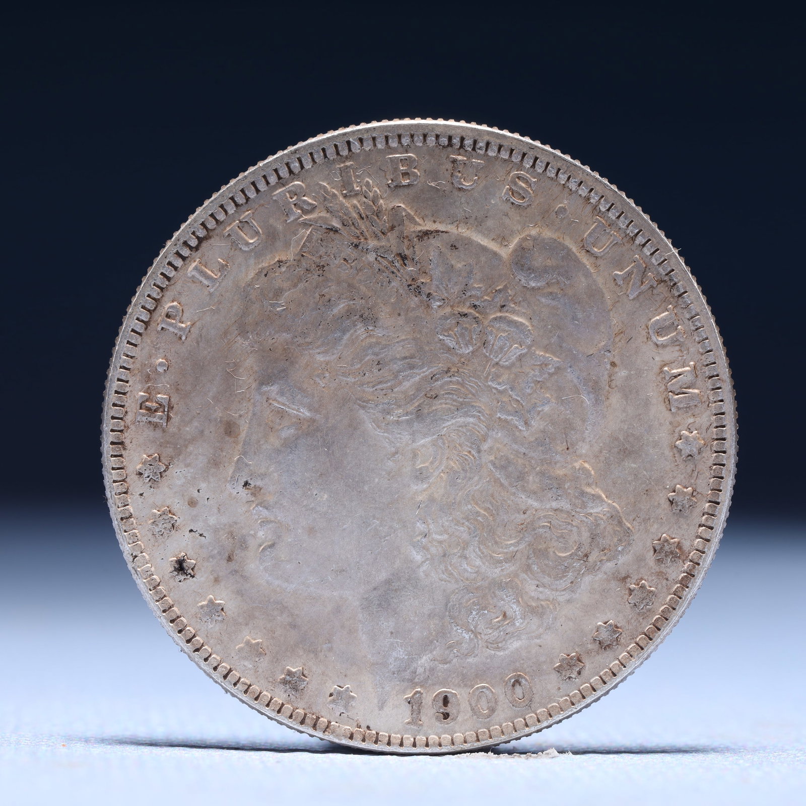USA Morgan Dollar 1900 Coin: Obv: profile bust with date below and E PLURIBUS UNUM legend and stars around. Rev: eagle with In God we trust above within wreath with UNITED STATES OF AMERICA ONE DOLLAR legend. IN GOD WE TRUST / LI