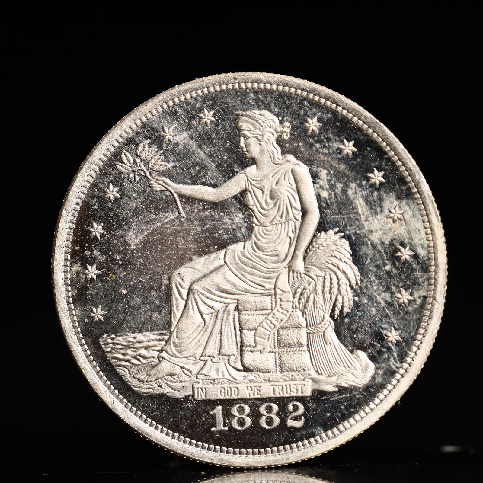 USA Trade Dollar 1882 Coin: American coin. Obverse: Liberty seated on a pedestal facing the sea to the left holding olive branches surrounded by 13 stars. IN GOD WE TRUST / LIBERTY / 1882. Reverse: An eagle holding branches with
