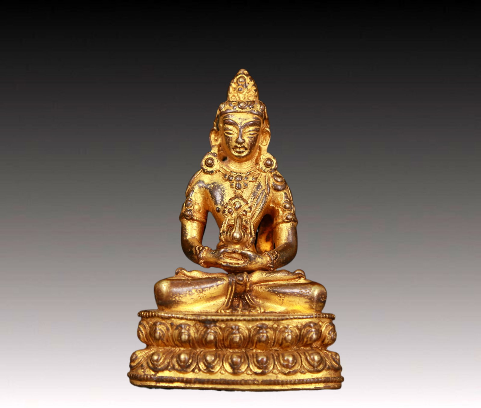 An exquisite gilt bronze statue of Amitayus Buddha: An exquisite gilt bronze statue of Amitayus Buddha,Ming Dynasty,China. The Buddha's face has clear outlines,deep eyes,a solemn and kind expression,and the corners of his mouth are slightly upturned,as