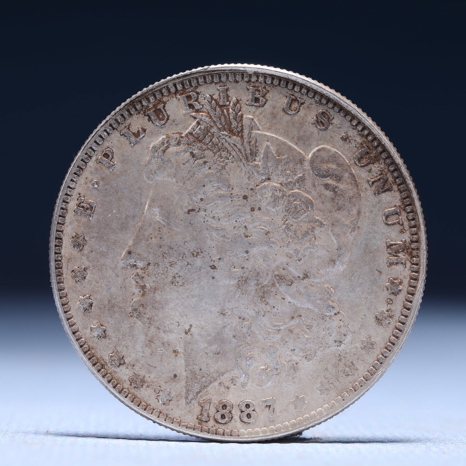 USA Morgan Dollar 1887 Coin: Obv: profile bust with date below and E PLURIBUS UNUM legend and stars around. Rev: eagle with In God we trust above within wreath with UNITED STATES OF AMERICA ONE DOLLAR legend. IN GOD WE TRUST / LI