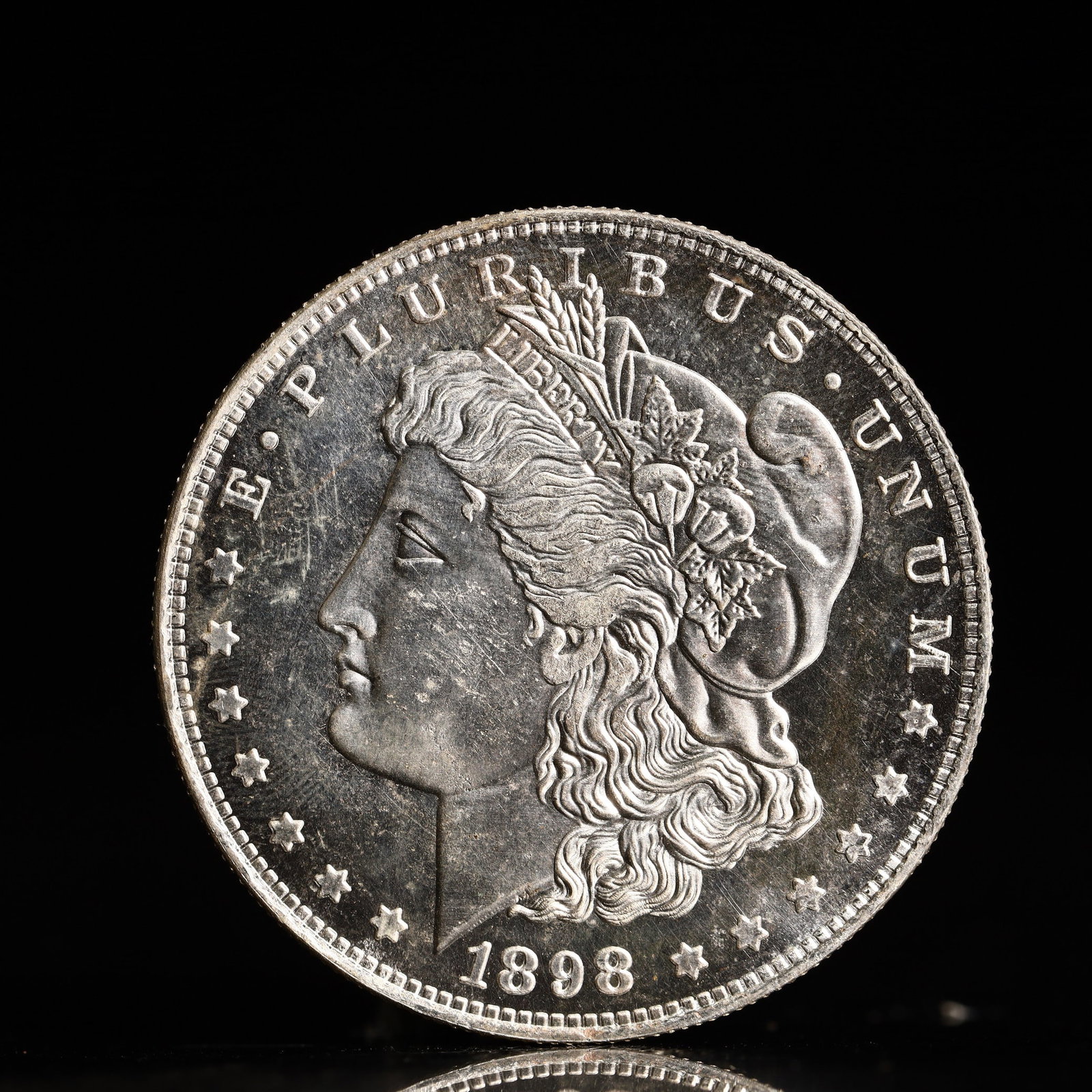 USA Morgan Dollar 1898 Coin: Obv: profile bust with date below and E PLURIBUS UNUM legend and stars around. Rev: eagle with In God we trust above within wreath with UNITED STATES OF AMERICA ONE DOLLAR legend. IN GOD WE TRUST / LI