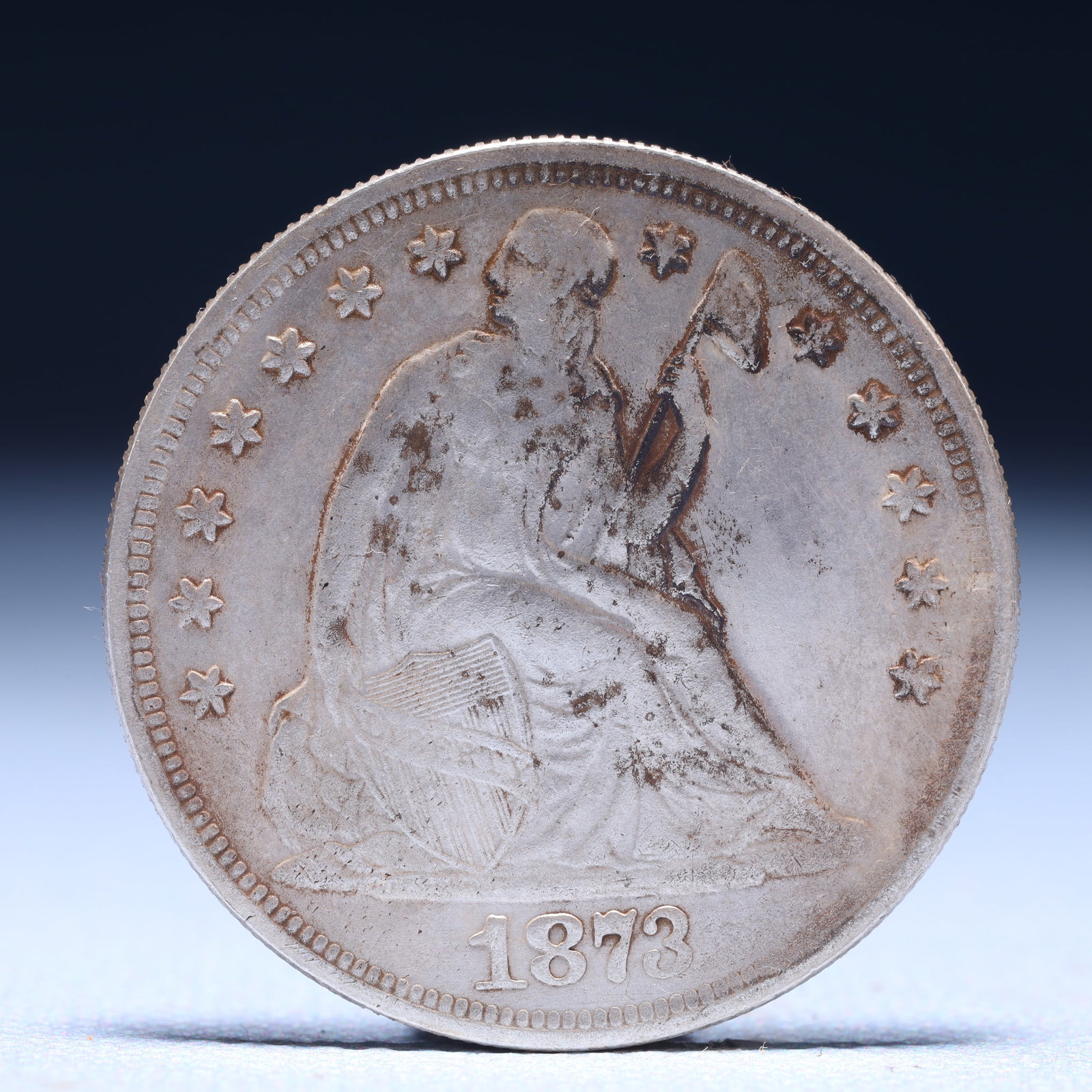 USA Trade Dollar 1873 Coin: American coin. Obverse: Liberty seated on a pedestal facing the sea to the left holding olive branches surrounded by 13 stars. IN GOD WE TRUST / LIBERTY / 1873. Reverse: An eagle holding branches with