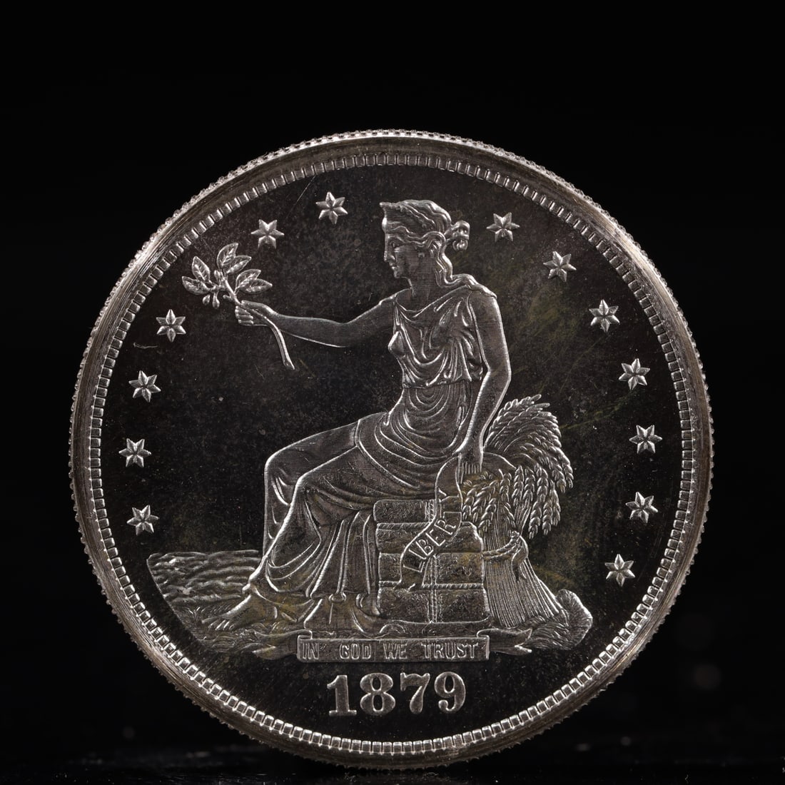 USA Trade Dollar 1879 Coin: American coin. Obverse: Liberty seated on a pedestal facing the sea to the left holding olive branches surrounded by 13 stars. IN GOD WE TRUST / LIBERTY / 1879. Reverse: An eagle holding branches with