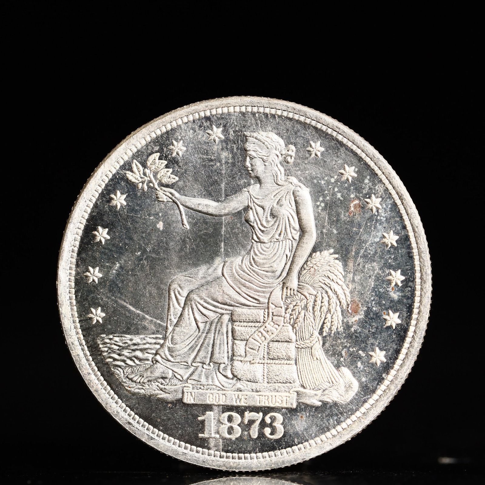 USA Trade Dollar 1873 Coin: American coin. Obverse: Liberty seated on a pedestal facing the sea to the left holding olive branches surrounded by 13 stars. IN GOD WE TRUST / LIBERTY / 1873. Reverse: An eagle holding branches with