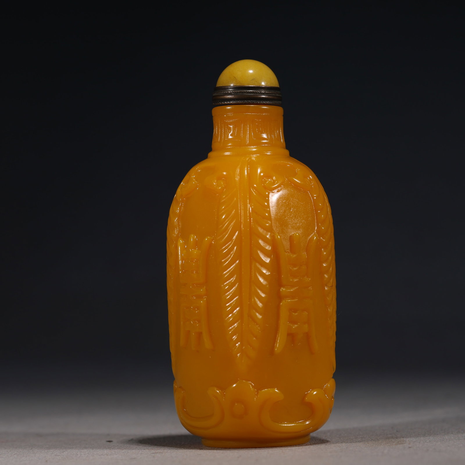 A Chinese Yellow Glass Snuff Bottle Carved with Archaistic Motifs,Qianlong Mark: A Chinese opaque yellow glass snuff bottle of cylindrical form,intricately carved with bands of ruyi heads and stylized archaistic patterns.It is fitted with a yellow glass stopper.The base bears a fo