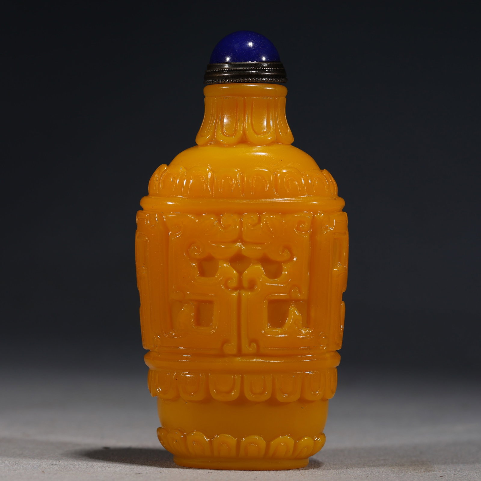 A Chinese Yellow Glass Snuff Bottle with Archaistic Motifs,Qianlong Mark: An opaque yellow glass snuff bottle of cylindrical form,carved in relief with stylized archaistic patterns within a rectangular panel,bordered by petal and ruyi-head bands at the neck,shoulder,and bas