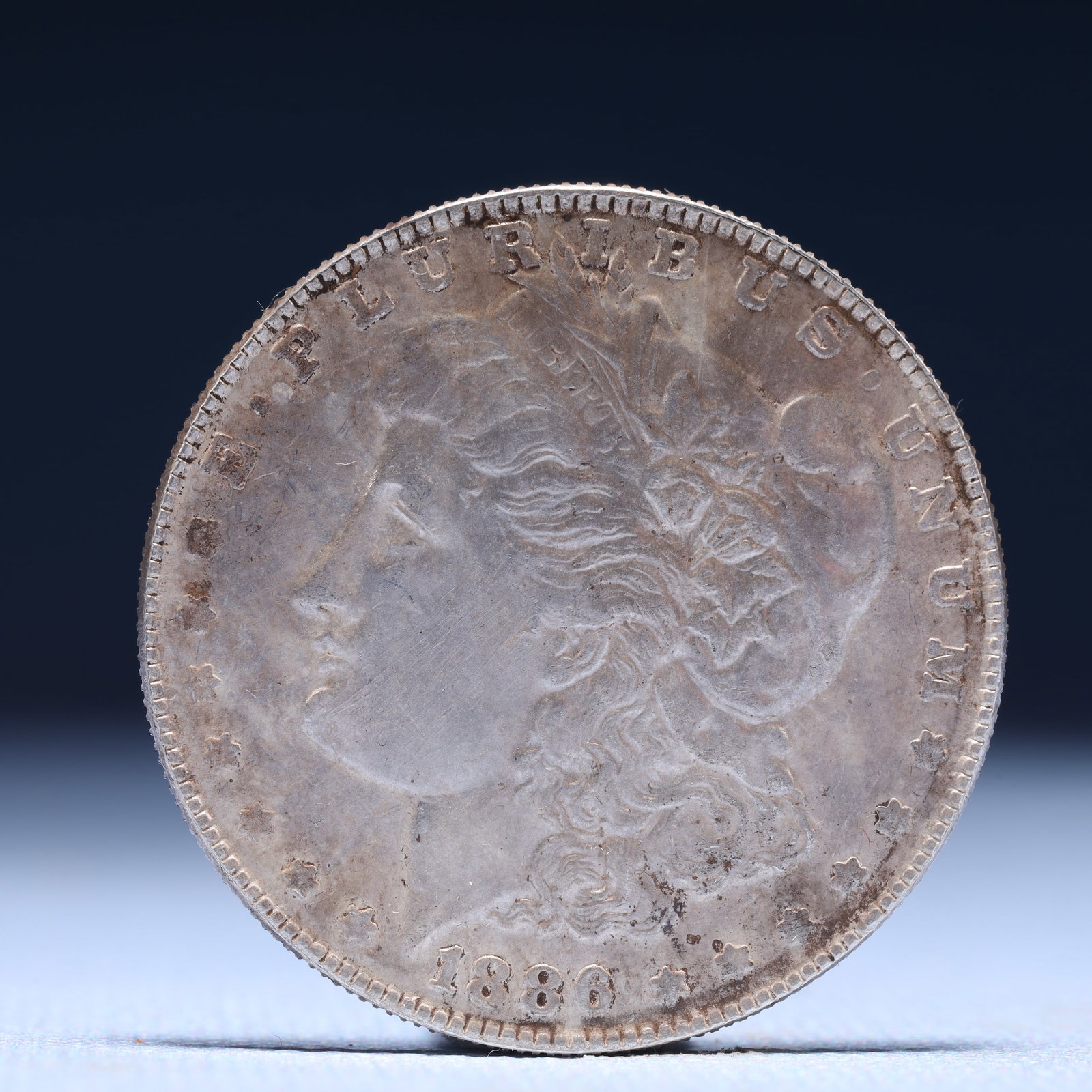 USA Morgan Dollar 1886 Coin: Obv: profile bust with date below and E PLURIBUS UNUM legend and stars around. Rev: eagle with In God we trust above within wreath with UNITED STATES OF AMERICA ONE DOLLAR legend. IN GOD WE TRUST / LI