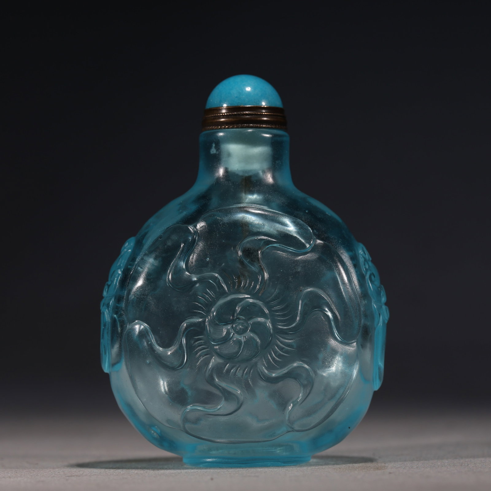 A Chinese Blue Glass Snuff Bottle with Mythical Beast,Qianlong Mark: A translucent blue glass snuff bottle,carved in relief with a crouching mythical beast amidst swirling clouds.Fitted with a turquoise glass stopper.The base bears a four-character seal mark reading(Qi