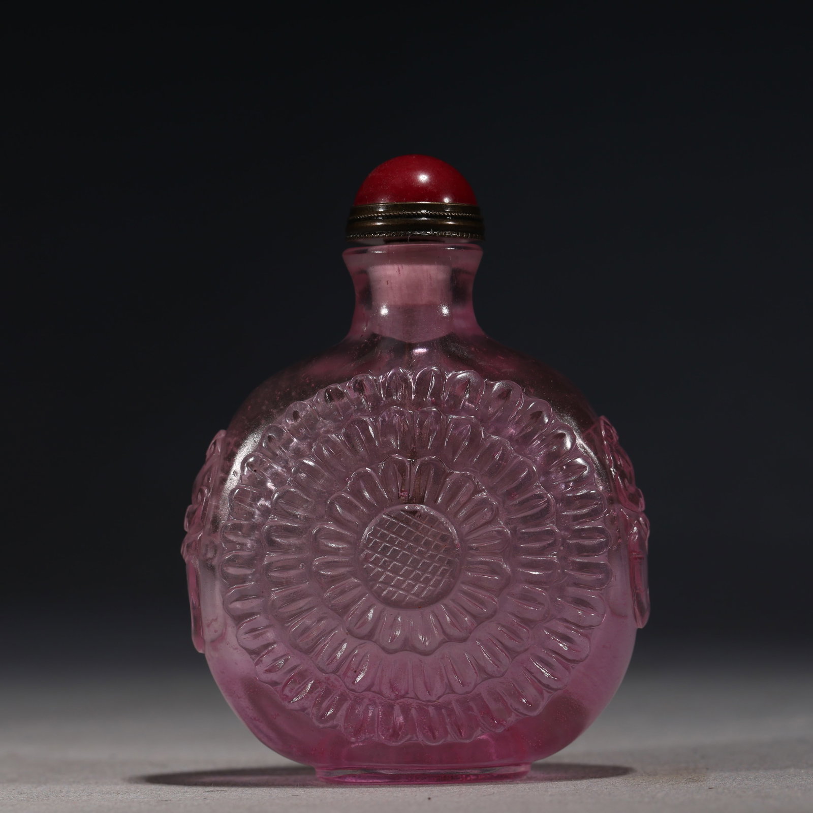A Chinese Pink Glass Snuff Bottle with Chrysanthemums,Qianlong Mark: A translucent pink glass snuff bottle of rounded form,deeply carved with a large chrysanthemum flower head.Fitted with a red glass stopper.The base bears a four-character seal mark reading(Qianlong Ni