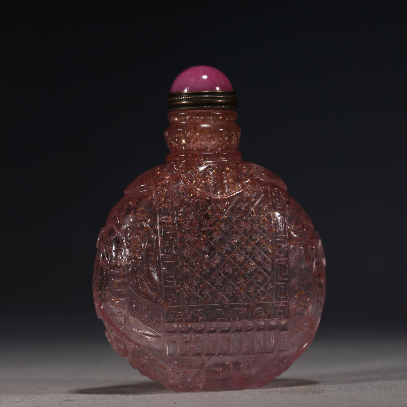 A Chinese Pink Gold-Speckled Glass Snuff Bottle with Diaper Pattern,Qianlong Mark: A translucent pink glass snuff bottle suffused with gold speckles,carved with a central diaper pattern within key-fret borders.Fitted with a pink stopper.The base bears a four-character seal mark read