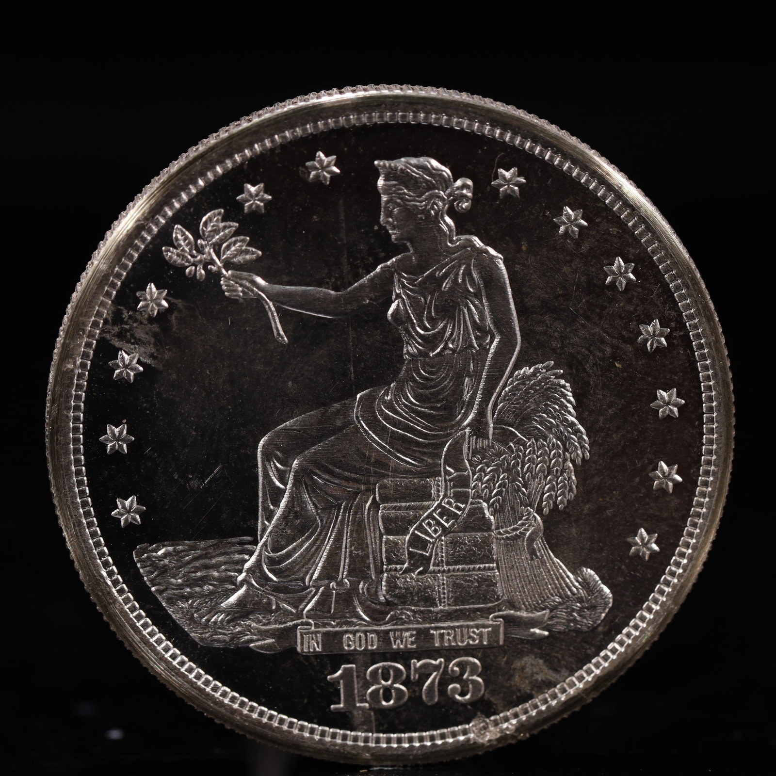 USA Trade Dollar 1873 Coin: American coin. Obverse: Liberty seated on a pedestal facing the sea to the left holding olive branches surrounded by 13 stars. IN GOD WE TRUST / LIBERTY / 1873. Reverse: An eagle holding branches with