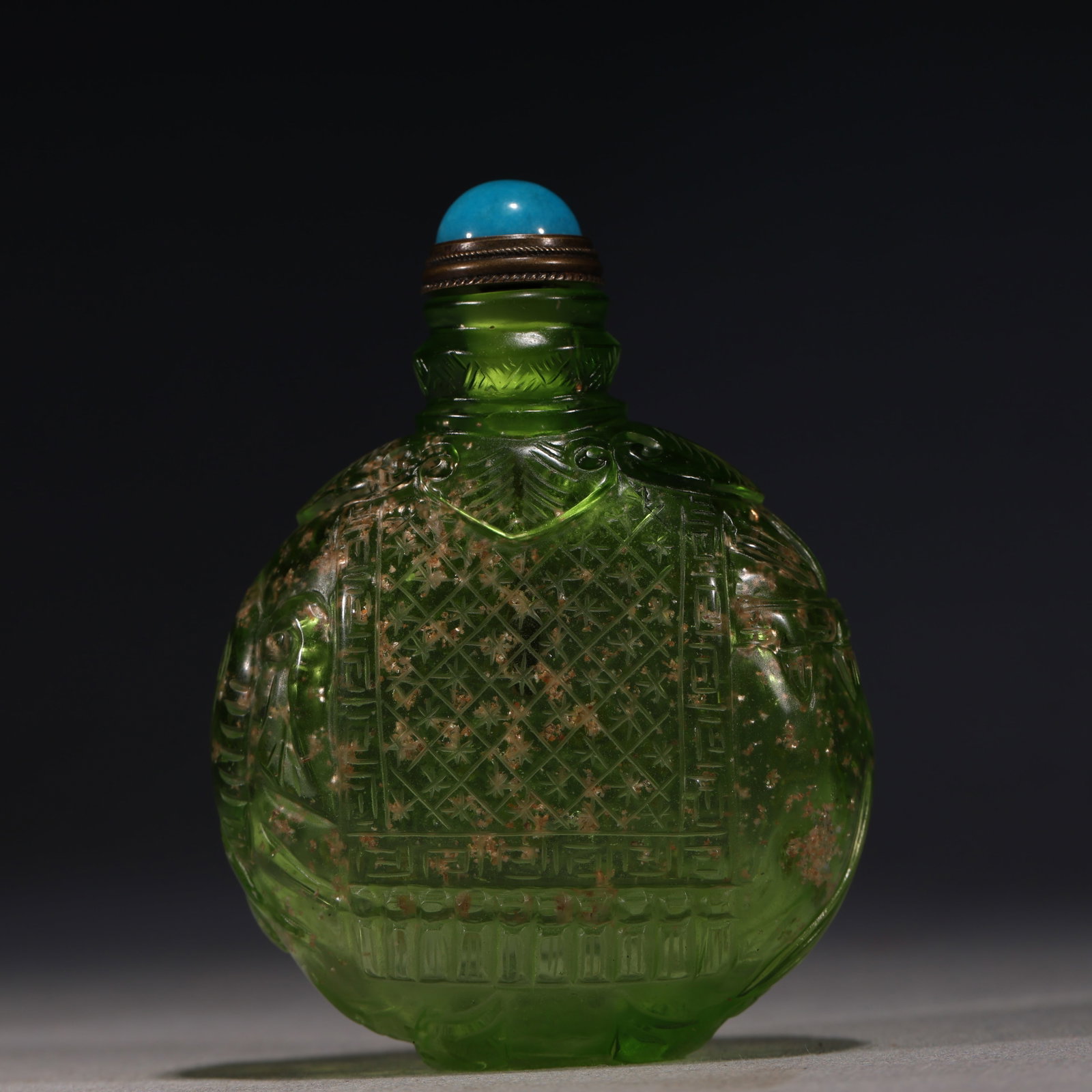 A Chinese Green Gold-Speckled Glass Snuff Bottle with Diaper Pattern,Qianlong Mark: A translucent green glass snuff bottle suffused with gold speckles,carved with a star diaper panel surrounded by key-fret borders.Fitted with a turquoise glass stopper.The base bears a four-character 