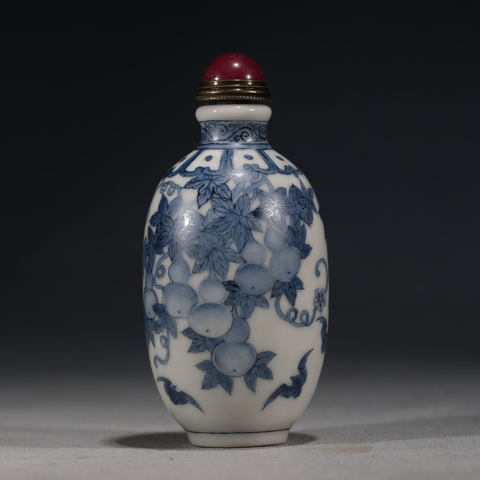 A Chinese Blue and White Porcelain Snuff Bottle with Gourds,Kangxi Mark: A blue and white porcelain snuff bottle of elongated ovoid form,painted with gourd vines and leaves,with bats flying below.Fitted with a red stopper.The base bears a four-character mark in underglaze 