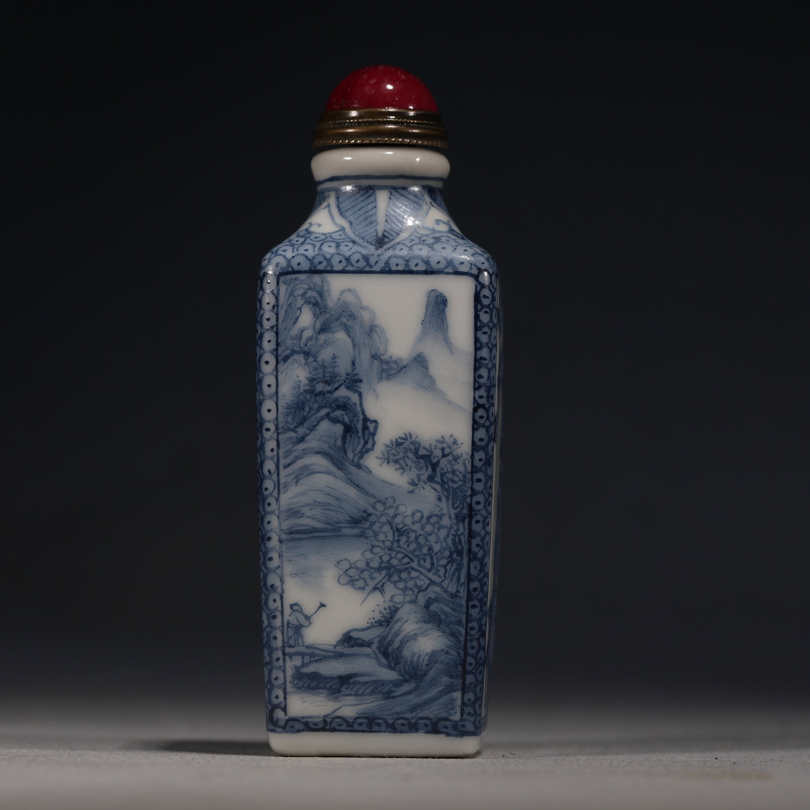 A Chinese Blue and White Porcelain Square Snuff Bottle with Birds,Butterflies and Landscape,Qianlong: A blue and white porcelain snuff bottle of square form,painted with a bird,butterflies and flowers on one face,and figures in a mountainous landscape on the other.Fitted with a red glass stopper.The b