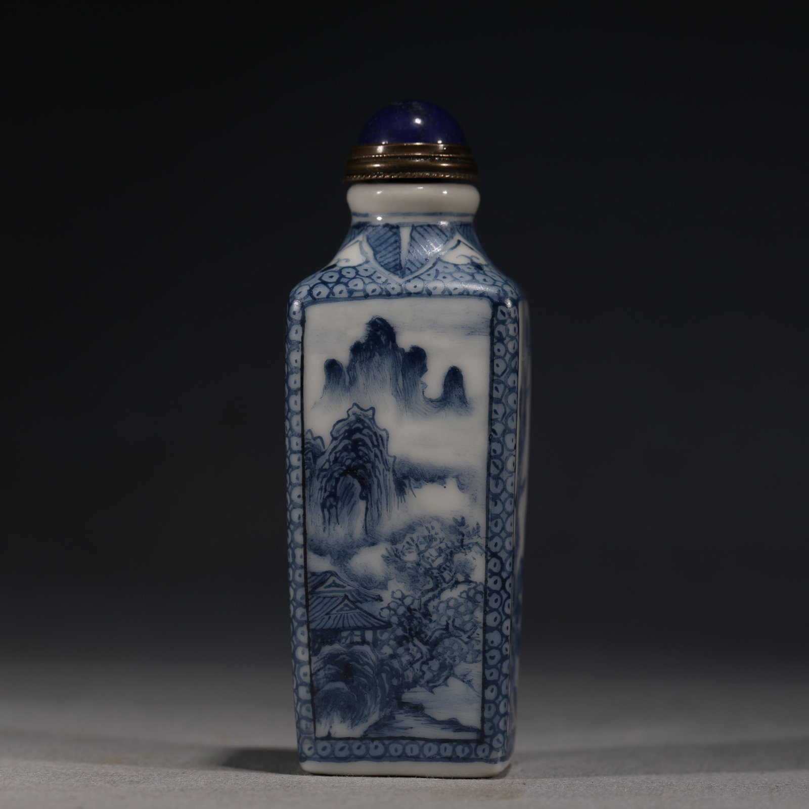 A Chinese Blue and White Porcelain Square Snuff Bottle with Landscape and Bamboo,Kangxi Mark: A blue and white porcelain snuff bottle of square form,painted with a landscape of mountains and pavilions on one side,and birds among bamboo and rockwork on the other.Fitted with a blue glass stopper
