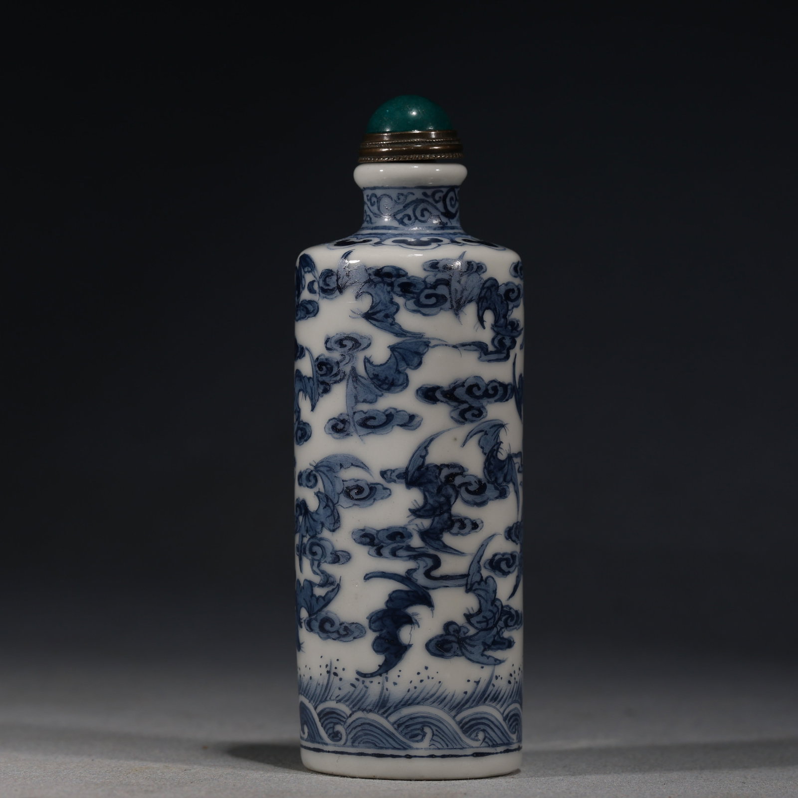 A Chinese Blue and White Porcelain Cylindrical Snuff Bottle with Clouds and Bats,Qianlong Mark: A blue and white porcelain snuff bottle of cylindrical form,painted with bats amidst clouds above a turbulent wave border.Fitted with a green glass stopper.The base bears a four-character seal mark re