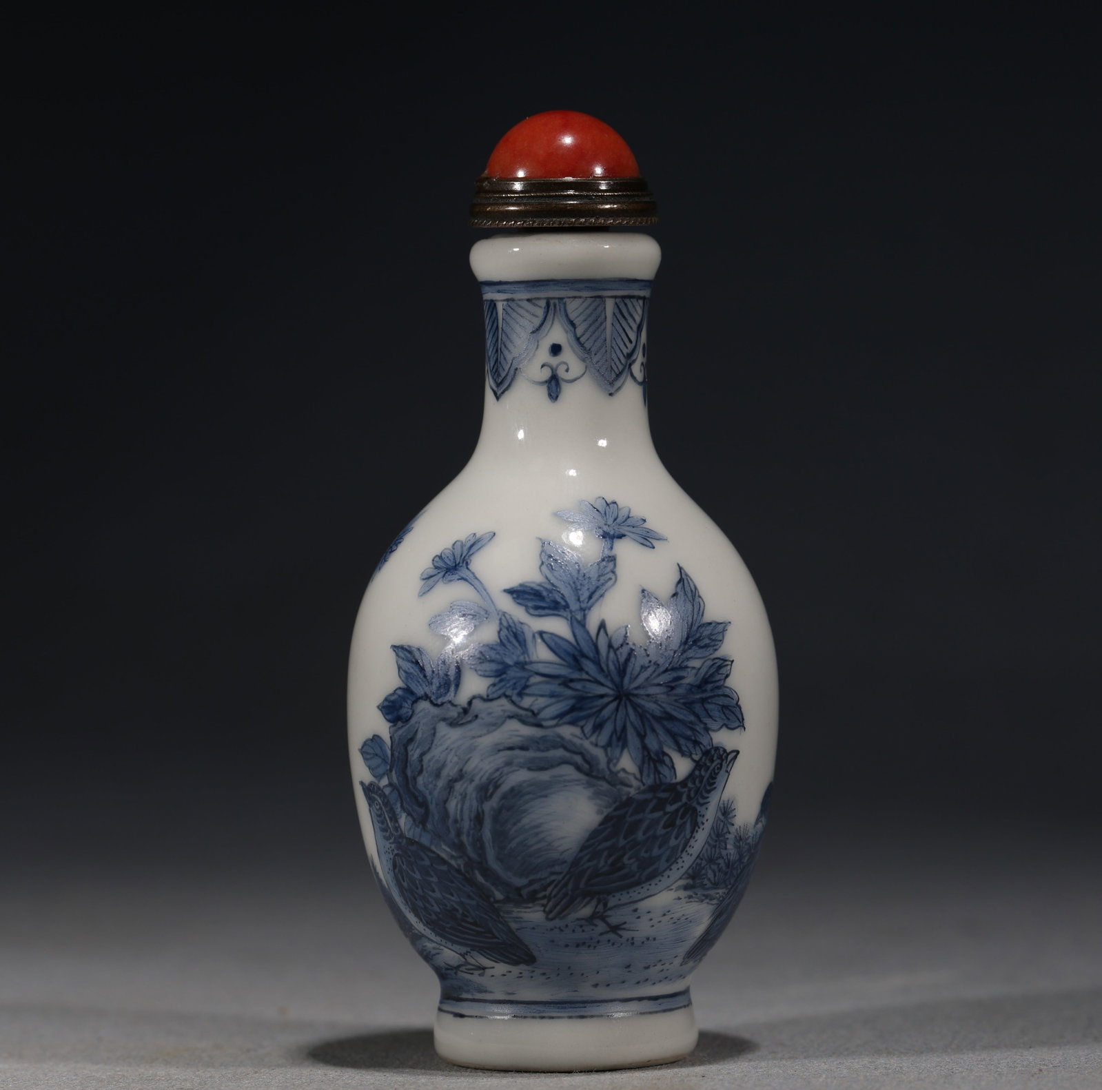 A Chinese Blue and White Porcelain Ovoid Snuff Bottle with Quails and Flowers,Qianlong Mark: A blue and white porcelain snuff bottle of ovoid form,painted with two quails beside rockwork and flowering plants.Fitted with a red glass stopper.The base bears a four-character seal mark reading(Qia