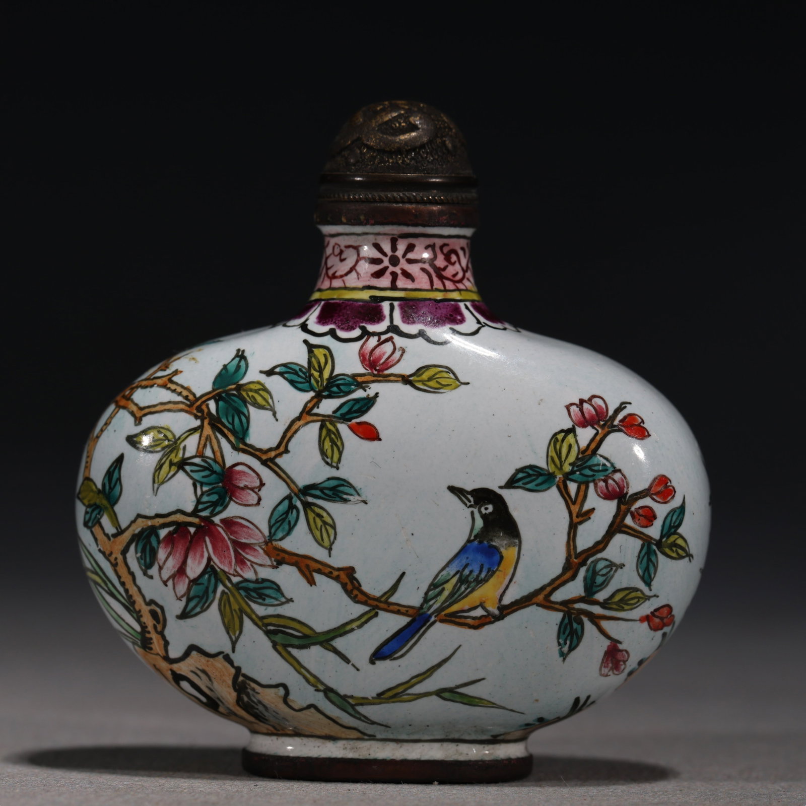 A Chinese Painted Enamel Snuff Bottle with Birds and Magnolia,Qianlong Mark: A Chinese white-ground painted enamel snuff bottle,decorated with a colorful bird perched on a flowering magnolia branch.Fitted with a bronze stopper.The base bears a four-character mark reading(Qianl