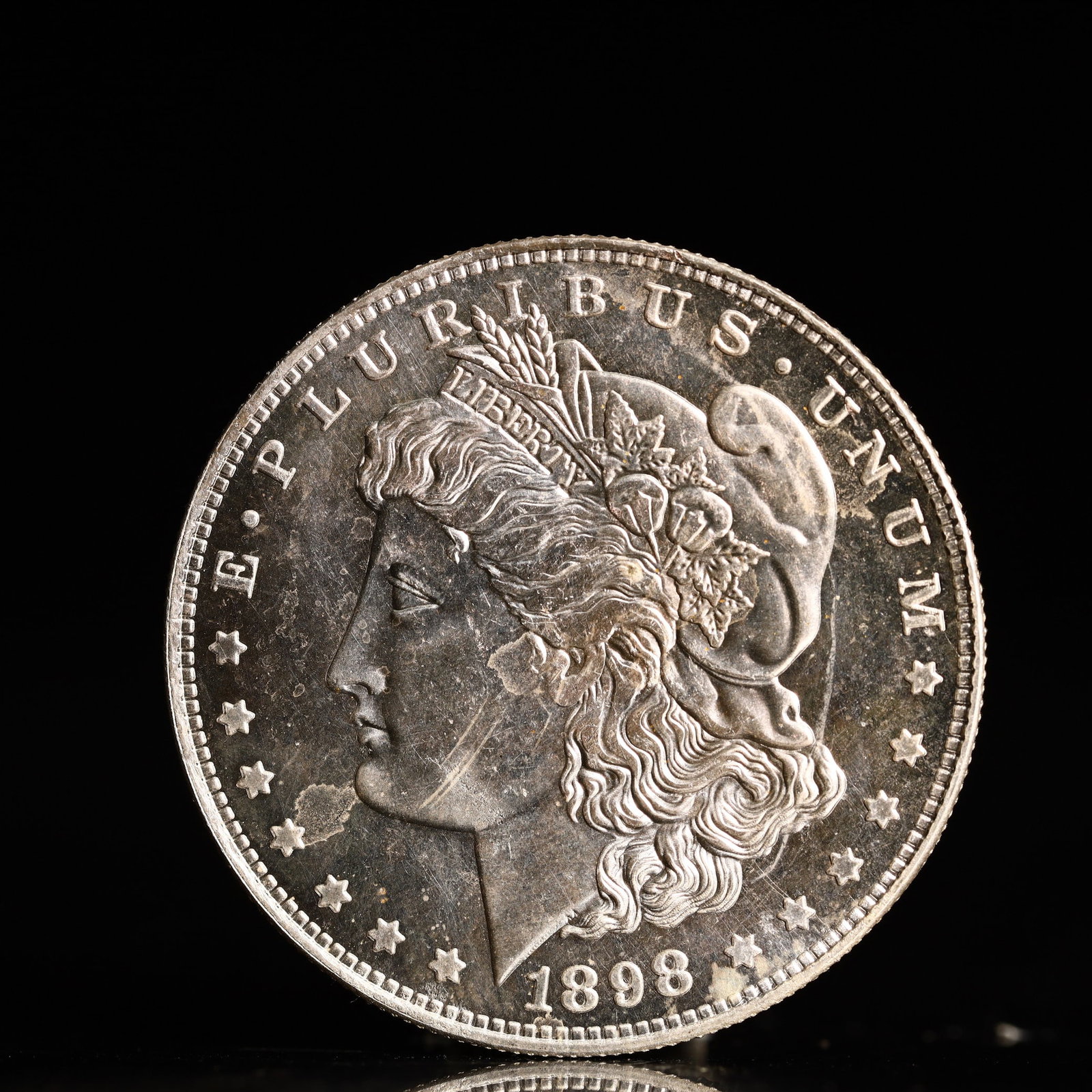 USA Morgan Dollar 1898 Coin: Obv: profile bust with date below and E PLURIBUS UNUM legend and stars around. Rev: eagle with In God we trust above within wreath with UNITED STATES OF AMERICA ONE DOLLAR legend. IN GOD WE TRUST / LI