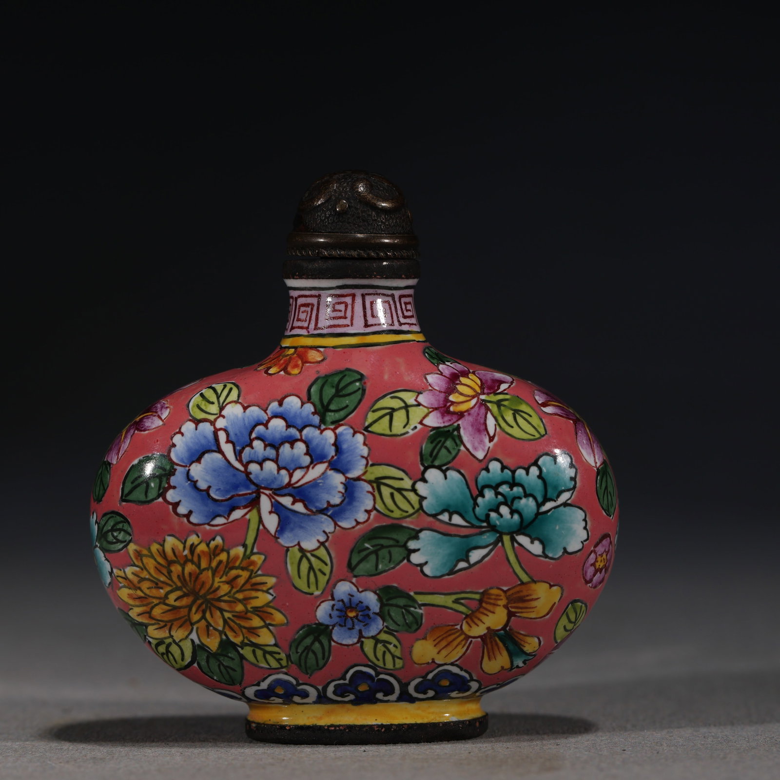 A Chinese Painted Enamel Snuff Bottle with Floral Sprays,Qianlong Mark: A Chinese pink-ground painted enamel snuff bottle,decorated with various blooming flowers including peonies and chrysanthemums.Fitted with a bronze stopper.The base bears a four-character mark