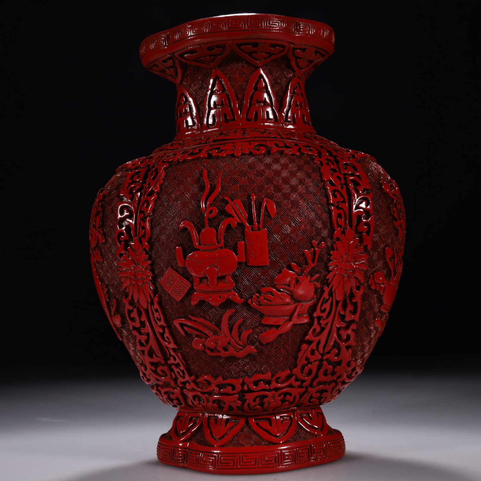 A Carved Cinnabar Lacquer Vase with Eight Buddhist Emblems and Antique Motifs: With a flared mouth, contracted neck, angular shoulders, bulbous belly, and a splayed ring foot. The body is banded with lotus scrolls and key-fret patterns. The main belly is carved with a 'Bogu' sce