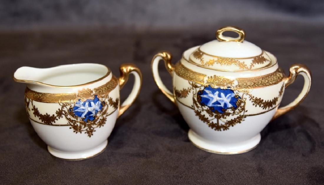 Noritake Gold Trimmed Porcelain Sugar and Creamer: Hand painted, each w/reserves having two white doves, covered sugar 5" tall & creamer 3 1/2" tall.