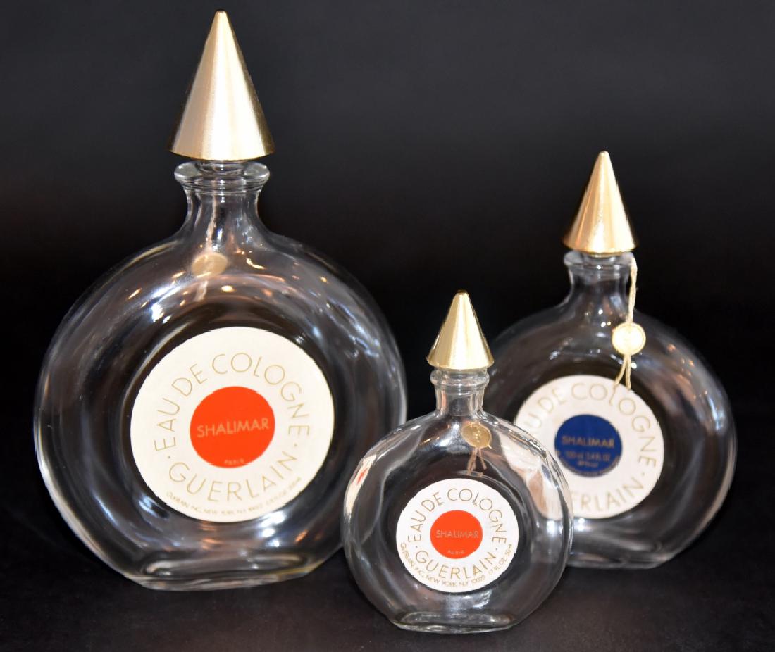 3 Shalimar Cologne Bottles: All w/gold button tags, largest 7.25" high w/red label & lightly embossed Guerlain Made in France, middle 5.5" high w/blue label embossed Guerlain and smallest 4.25" high w/red label embossed Guerlain