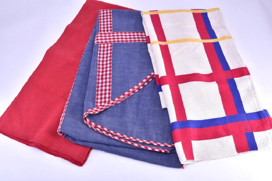 3 Red, Blue Tablecloths: Solid red tablecloth, 49 " long x 48" wide; red, yellow, blue & white tablecloth, 47" long X 38" wide; oval blue w/red & white squares tablecloth, 83" long x 60" wide.