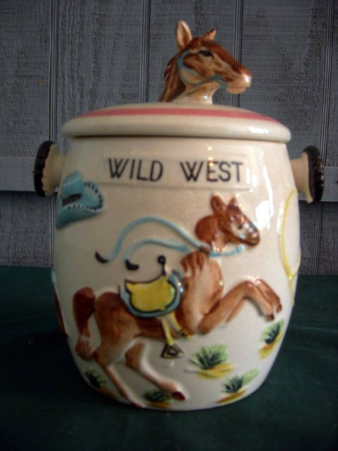 WILD WEST BISCUIT JAR: Wild West Biscuit Jar, Ivory w/Embossed Painted Horse, Hat, Lasso, Wagon, Rifle, Boots and Banjo. Lid has Horse Head Knob, 7.5" Tall.