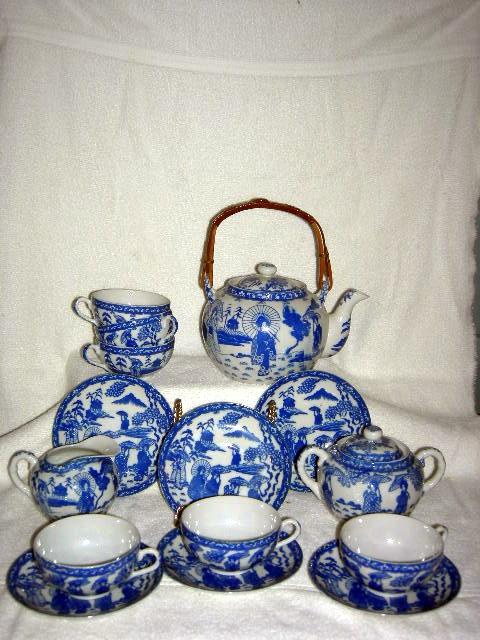 PORCELAIN ORIENTAL TEA SET: Oriental Tea Set w/Blue Figures on White Background Including Tea Pot w/Wicker Handle, 8.5" Tall, Creamer, 2.75" Tall, Covered Sugar, 4" Tall,6 Tea Cups and Saucers.