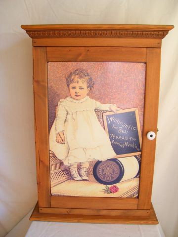 METAL FRONT CUPBOARD: Wood Storage Cupboard w/Metal Plate Front Depicting Little Girl, Large Spool of Thread & Chalkboard; Hinged Door w/Porcelain Pull & Metal Latch; 2 Wood Shelves. 15.5" W x 3.5" D x 22.5" T.