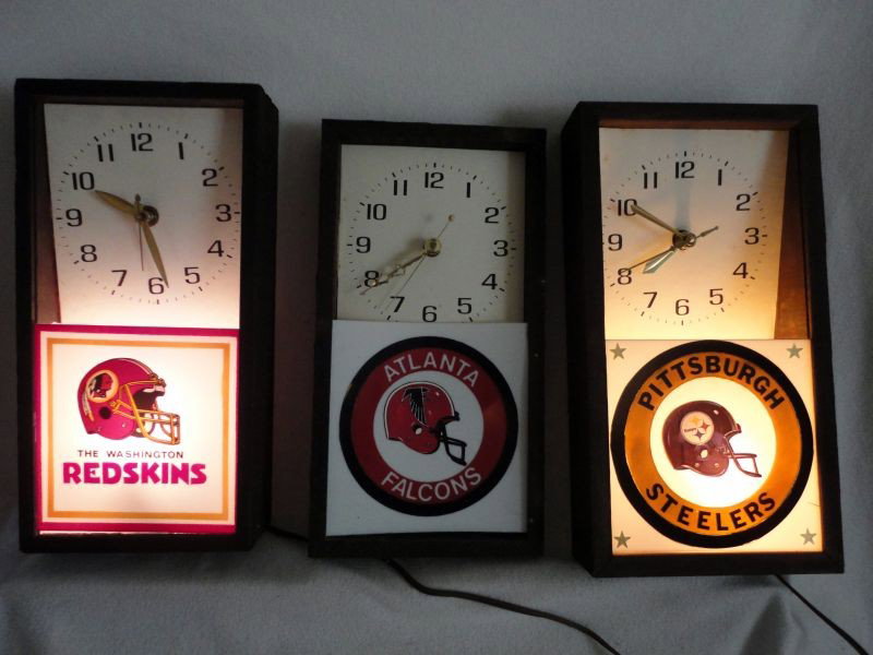 THREE WOOD FRAMED SPORTS CLOCKS: 3 Wood Framed Sports Advertising Clocks Inc. 2 Electric Lighted w/ "Lanshire Synchronous Self Starting Electric Clock Movement" Inc. "The Washington Redskins" & "Pittsburgh Steelers," 13.5"T & One Bat
