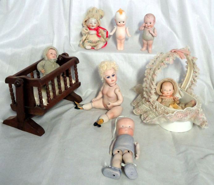 PORCELAIN DOLLS: Lot Includes 7 Reproduction Segmented Dolls w/1 Baby Doll in Bassinetand 1 in Rocking Cradle, a Kewpie Doll, Baby Bud, 2 More Babies and 1 Lady. 4.5" to 9" L.