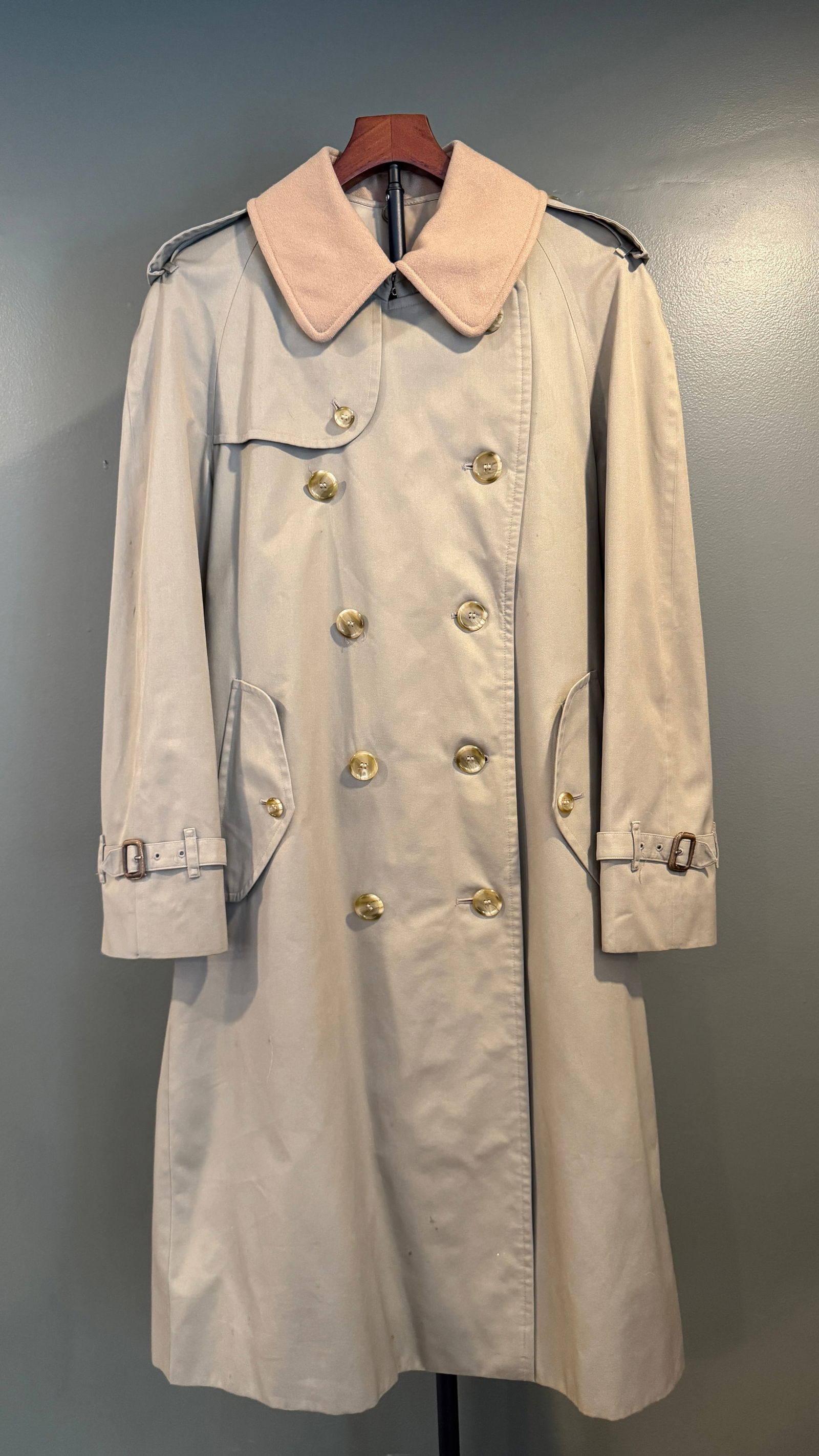Burberrys Trench Coat: A classic vintage trench coat by Burberrys, executed in a traditional double-breasted silhouette with epaulettes, storm flap, and adjustable cuff straps. Crafted in a neutral beige tone with a contras