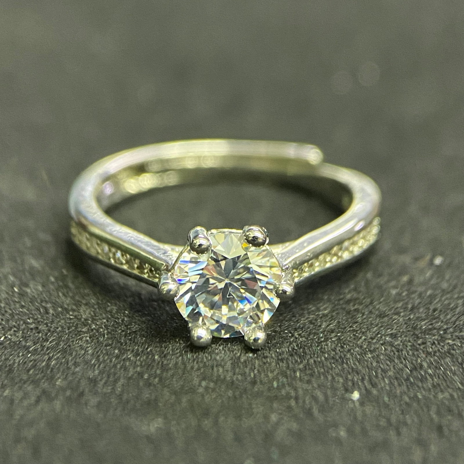 Elegant Round-Cut Solitaire Ring with Channel-Set Accents: A timeless solitaire ring featuring a brilliant round-cut center stone secured by a four-prong setting, flanked by channel-set accent stones in a polished silver-tone band.