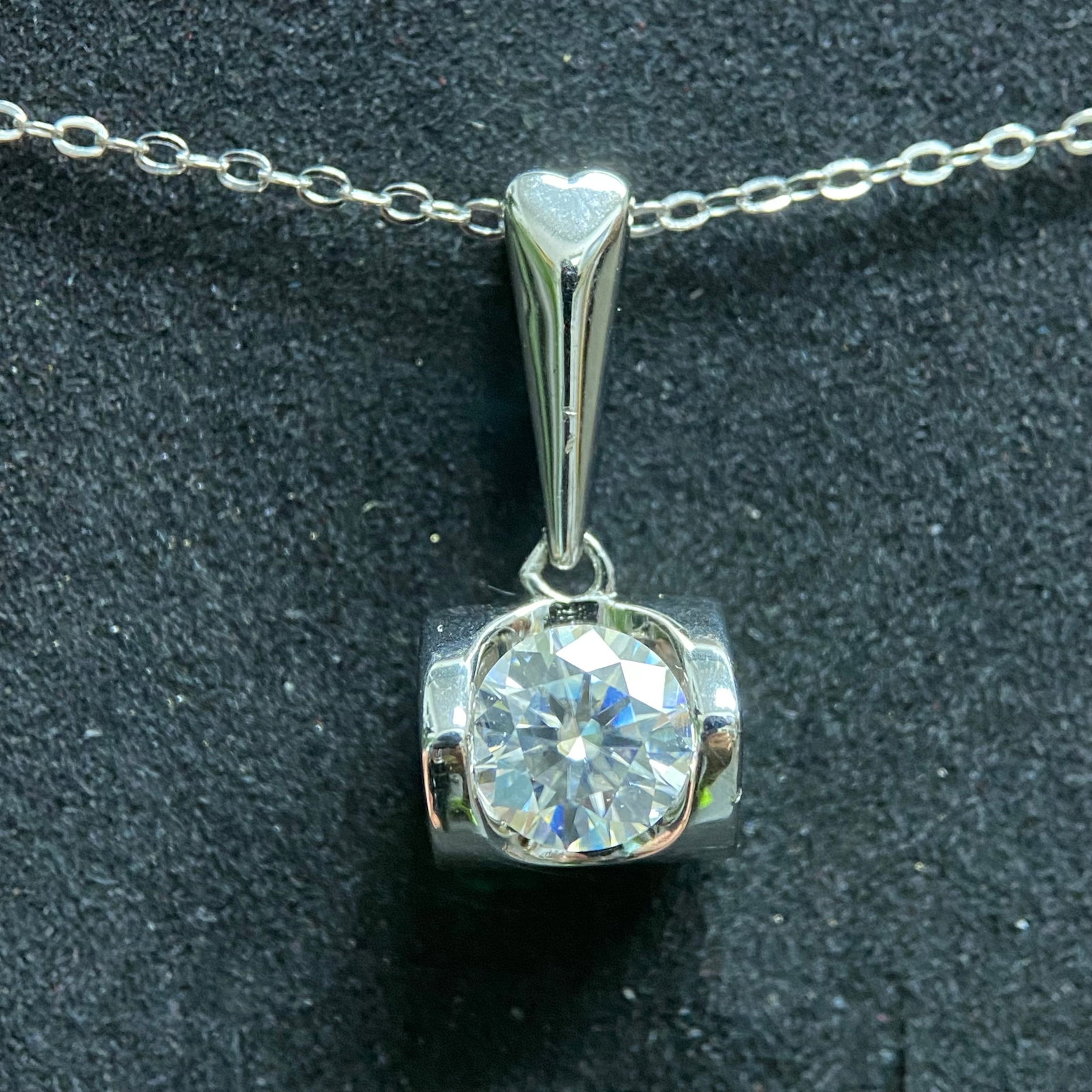 Minimalist Round-Cut Moissanite Pendant Necklace: A pair of elegant solitaire necklaces, each featuring a brilliant round-cut moissanite gemstone. The pendants are held in a classic four-prong setting and suspended from delicate, high-polished silver
