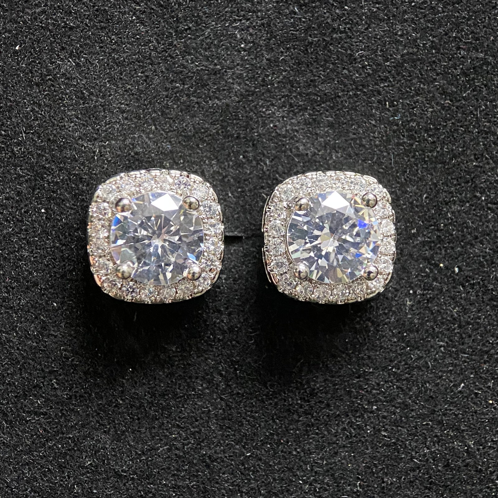 Classic Round-Cut Moissanite Stud Earrings: A pair of sophisticated stud earrings featuring brilliant round-cut moissanite gemstones. Each stone is secured by a classic four-prong basket setting in polished silver-tone metal, providing a timele