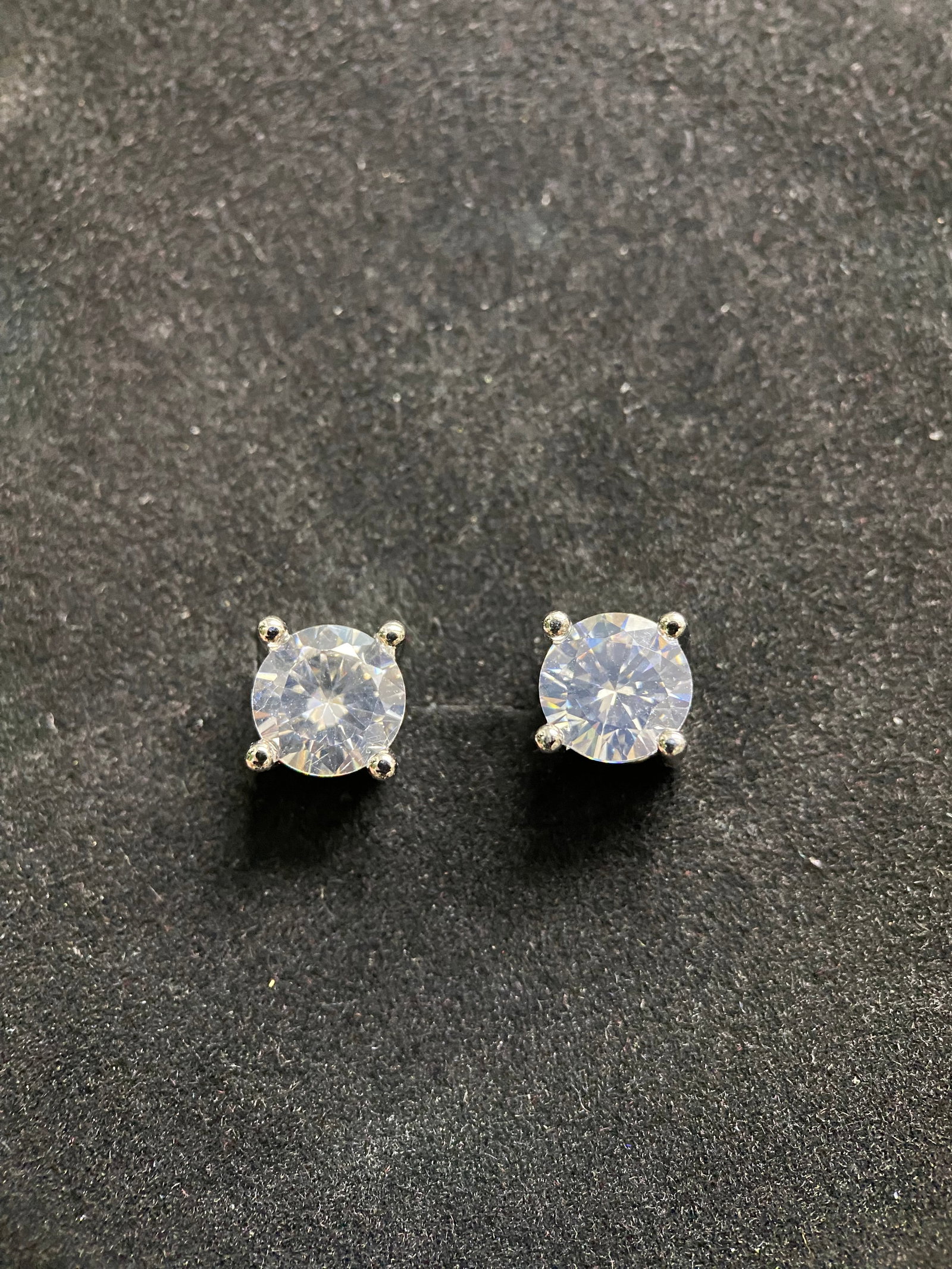 Classic Round-Cut Moissanite Stud Earrings: A pair of timeless stud earrings featuring brilliant round-cut moissanite gemstones. Each stone is secured by a classic four-prong setting in polished silver-tone metal, designed to maximize the stone