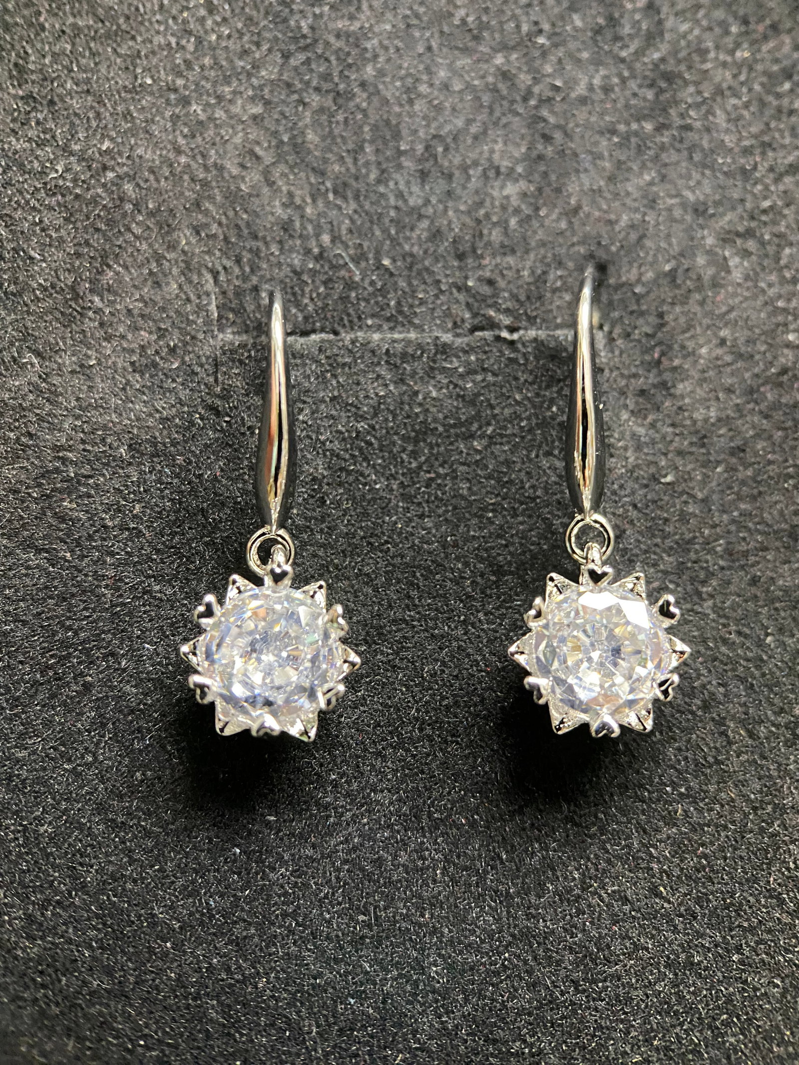 Classic Round-Cut Moissanite Stud Earrings: A pair of sophisticated stud earrings featuring brilliant round-cut moissanite gemstones. Each stone is secured by a classic four-prong basket setting in polished silver-tone metal, providing a timele
