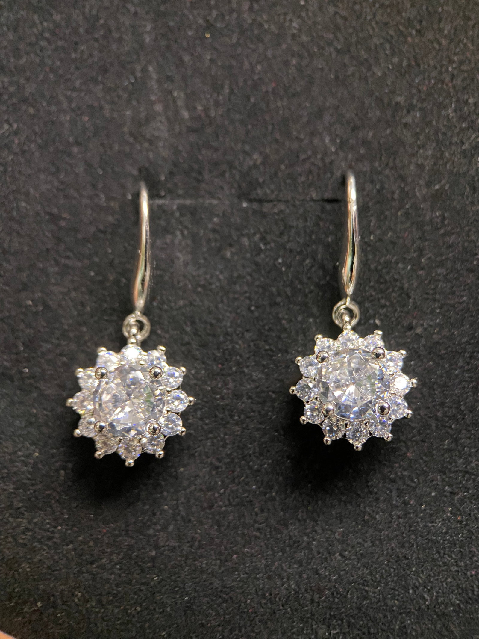 Classic Round-Cut Moissanite Stud Earrings: A pair of sophisticated stud earrings featuring brilliant round-cut moissanite gemstones. Each stone is secured by a classic four-prong basket setting in polished silver-tone metal, providing a timele
