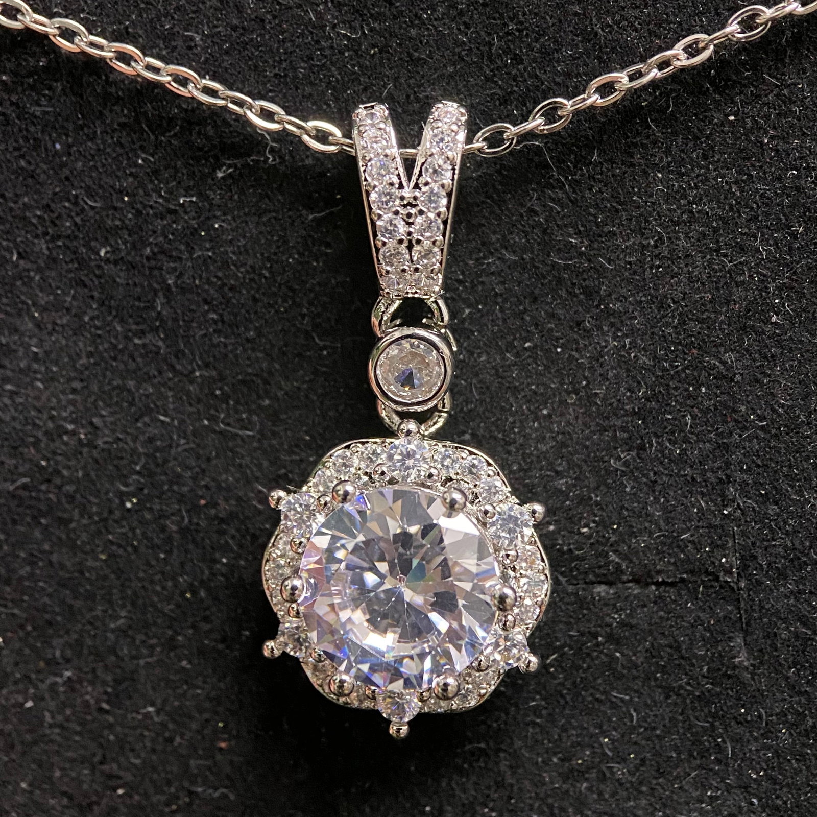 Moissanite Necklace – 3.0ct D Color, 9.0mm Round Brilliant – GRA Certified. Floral Halo Pendant.: This striking necklace features a brilliant 3.0-carat round moissanite center stone encased in a decorative floral-style halo setting with vintage-inspired prongs. The pendant is suspended from a pav�