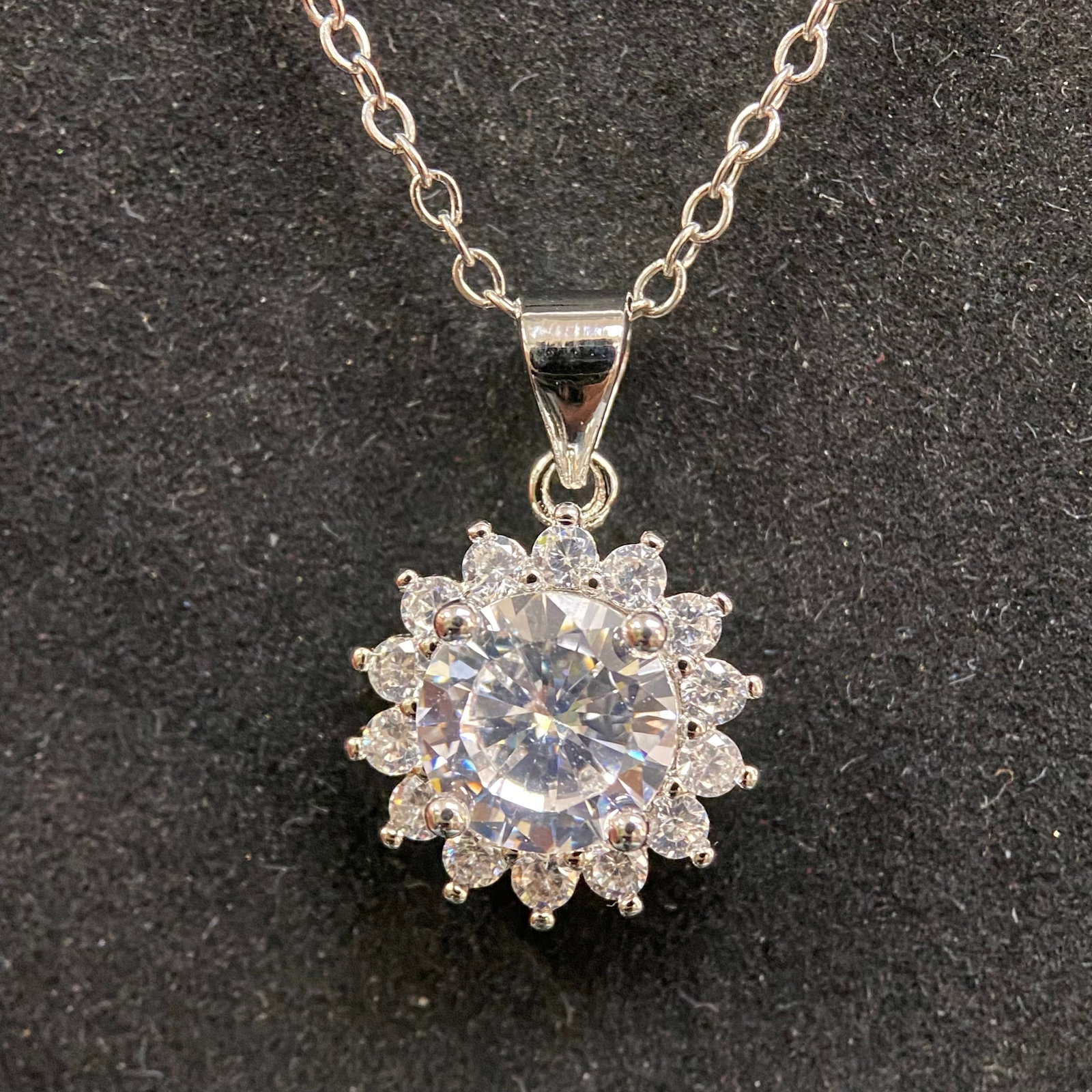 Moissanite Necklace – 1.0ct D Color, 6.5mm Round Brilliant – GRA Certified. Square Pavé Halo.: This elegant necklace features a 1.0-carat round brilliant moissanite center stone, securely held by four prongs within a sophisticated square-shaped halo. The halo is meticulously pavé-set with shim