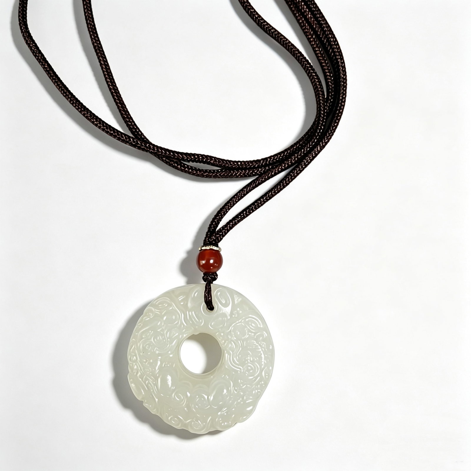 Hetian Jade Circular Pendant Necklace: Pendant necklace featuring a carved circular Hetian jade pendant suspended from a braided cord necklace with decorative bead accent. Traditional inspired design.