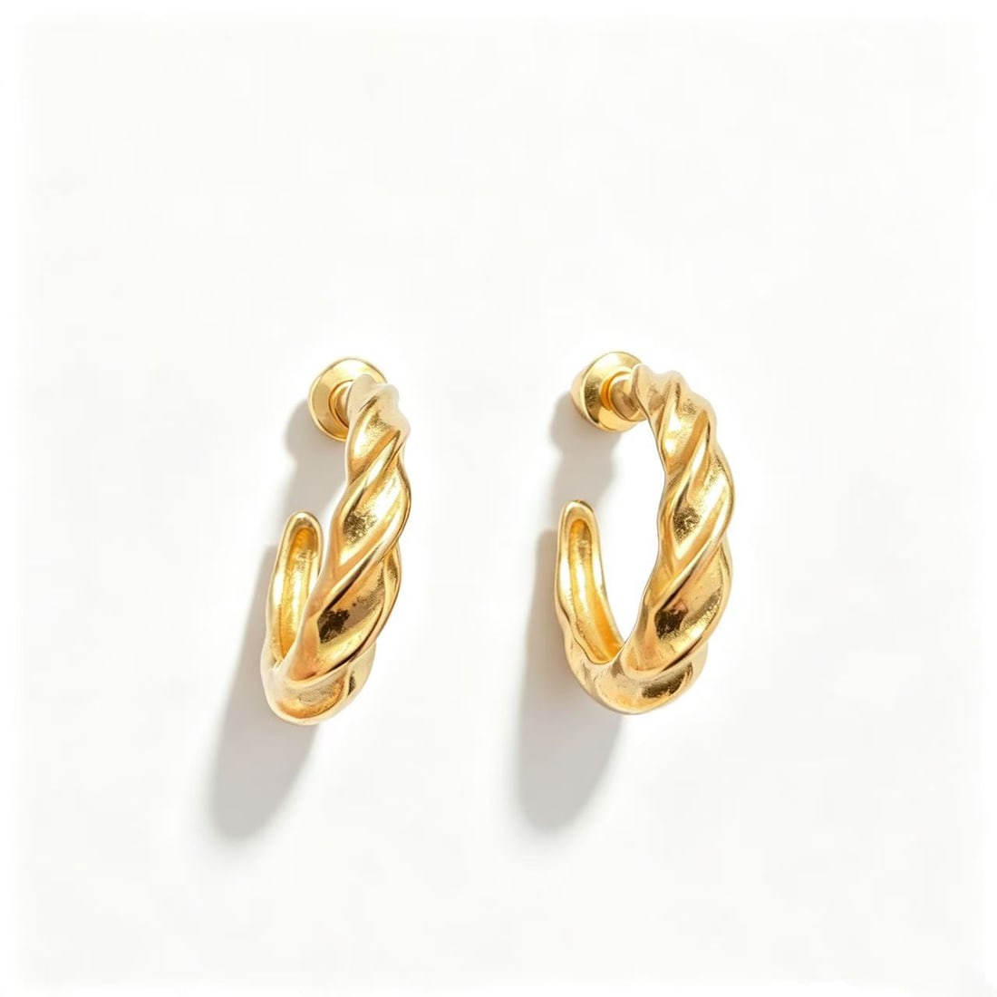 Gold-Gilded Twisted Hoop Earrings: Pair of twisted hoop earrings featuring a polished gold-gilded finish and sculptural intertwined design. Minimalist contemporary style.