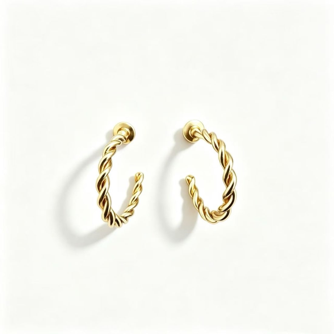 Gold-Gilded Twisted Hoop Earrings: Pair of twisted hoop earrings featuring a polished gold-gilded finish and sculptural intertwined design. Minimalist contemporary style.