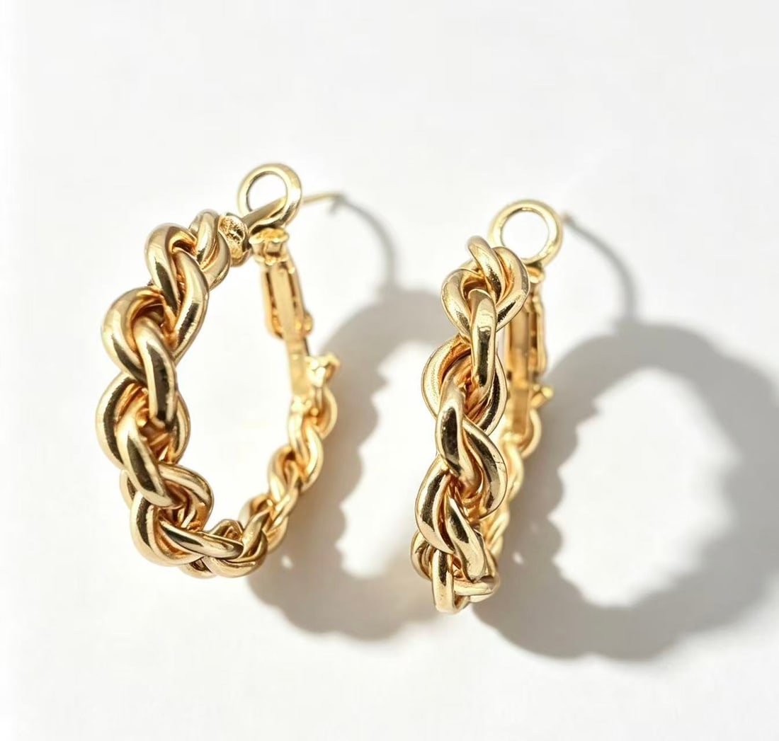 Gold-Gilded Chain Hoop Earrings: Pair of hoop earrings featuring an interwoven chain-style design with polished gold-gilded finish. Contemporary ornamental style