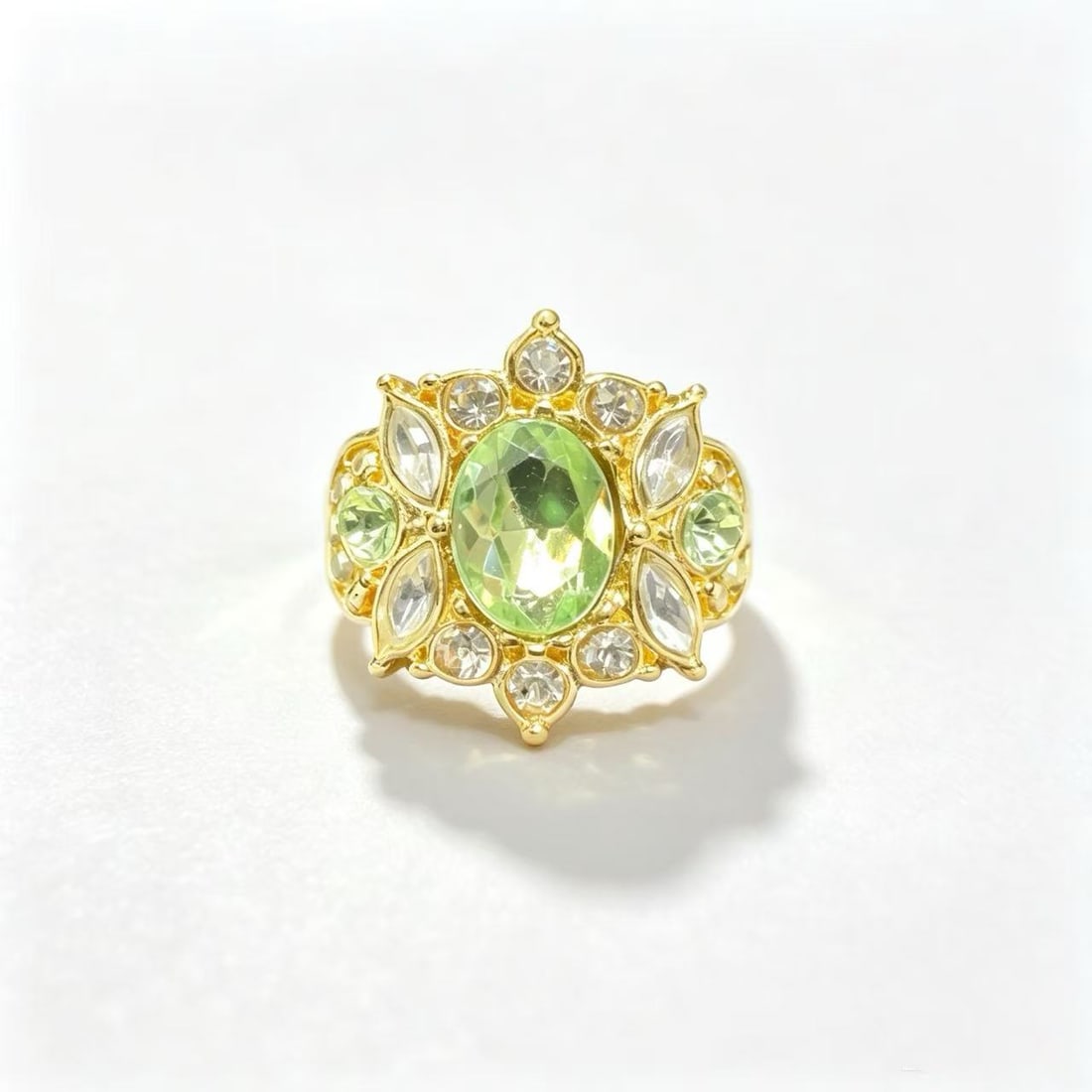 Olivine-Colored Gemstone Gold-Gilded Ring: Decorative ring featuring an olivine-colored center gemstone accented by clear and matching side stones with gold-gilded finish. Ornamental floral-inspired design.